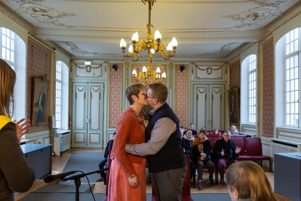 A romantic moment shared in an elegant historic room with ornate decor and chandeliers.