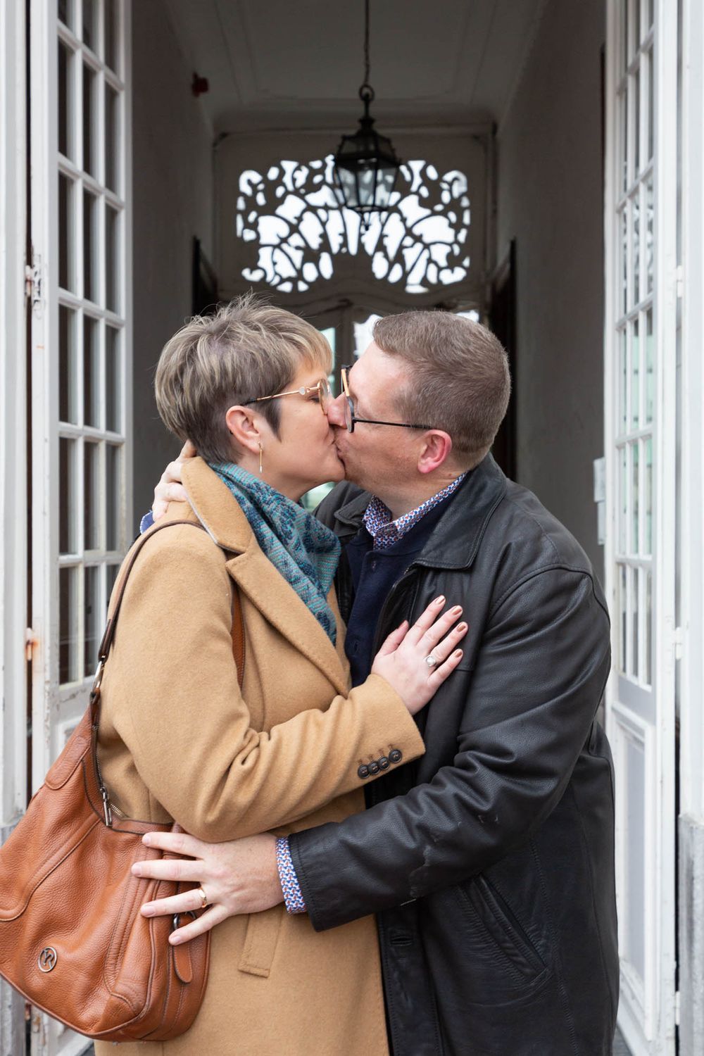 A couple sharing a romantic kiss in a doorway with ornate glass detail above.