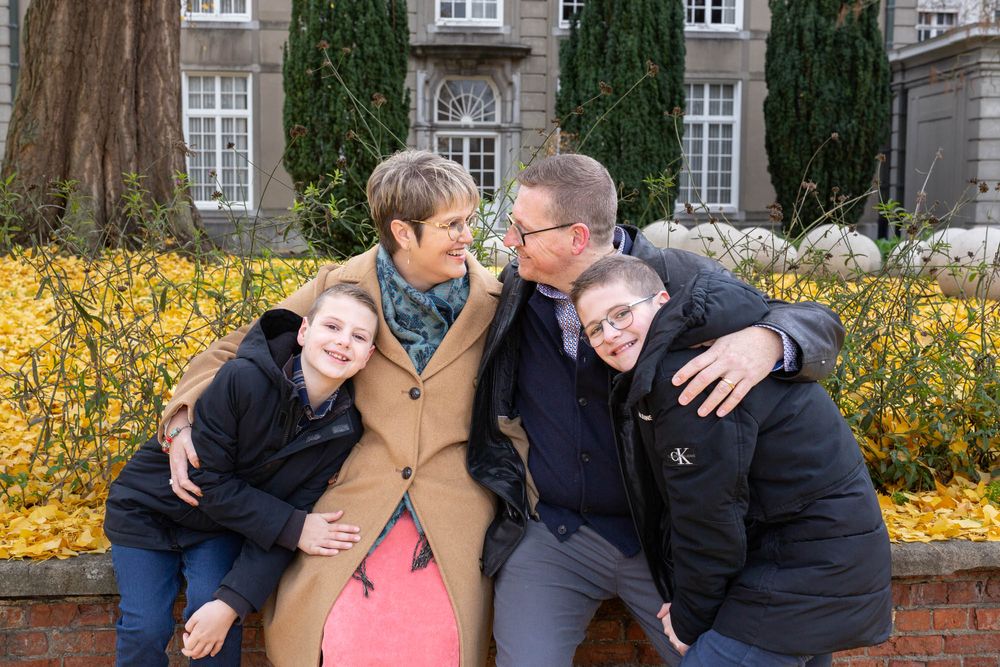 A family poses together on a brick wall with yellow forsythia bushes and autumn leaves.