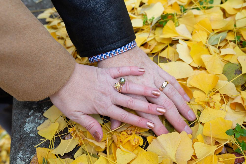 Two hands with rings rest together on fallen yellow ginkgo leaves.