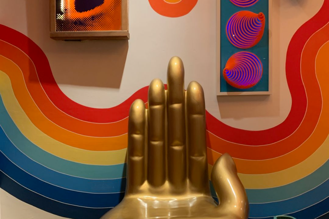 Gold hand sculpture against colorful rainbow wall art display.