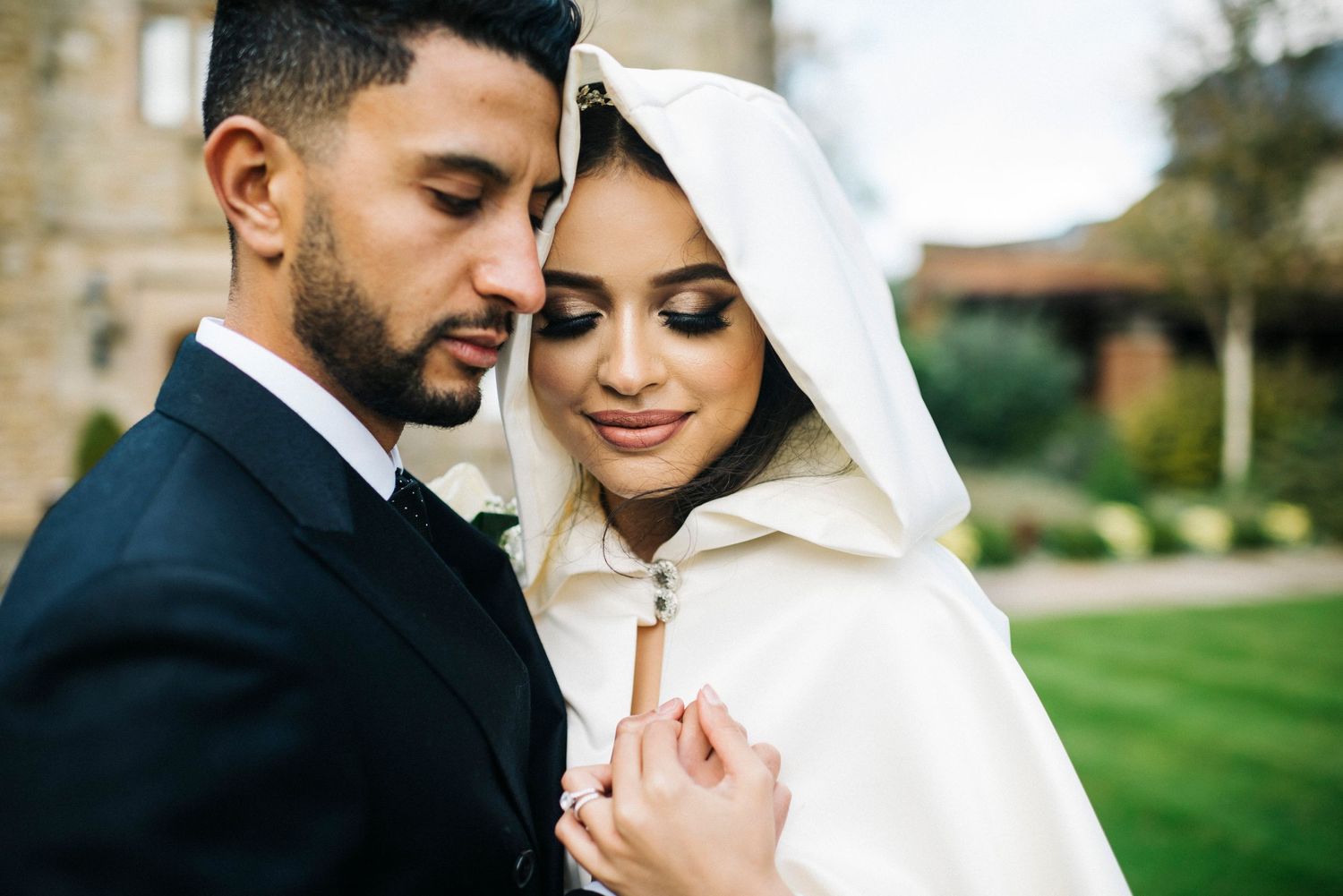 Intimate wedding portrait of couple embracing while bride wears elegant white hooded cape.