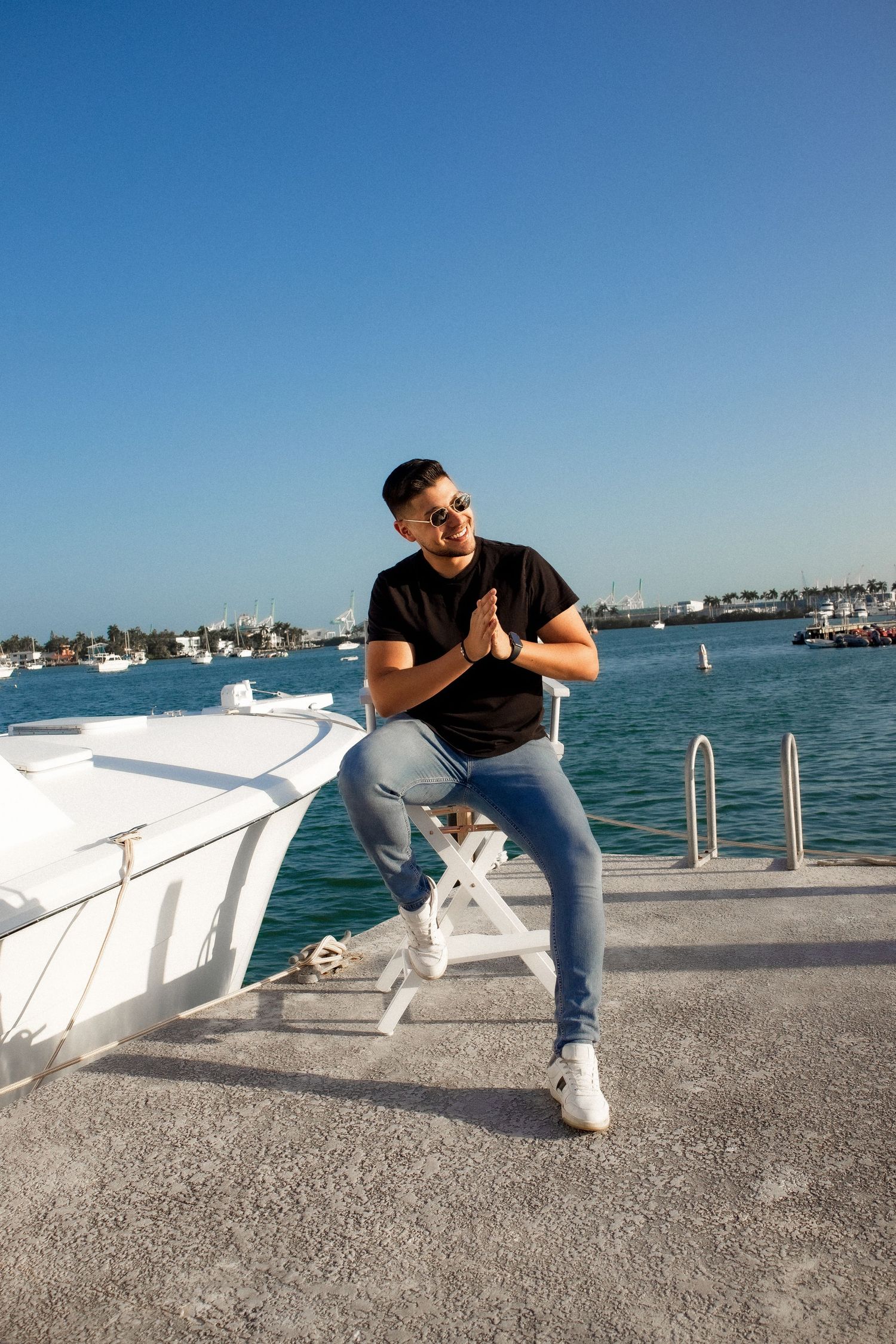 A casual-dressed person poses energetically on a white boat dock against a harbor backdrop.
