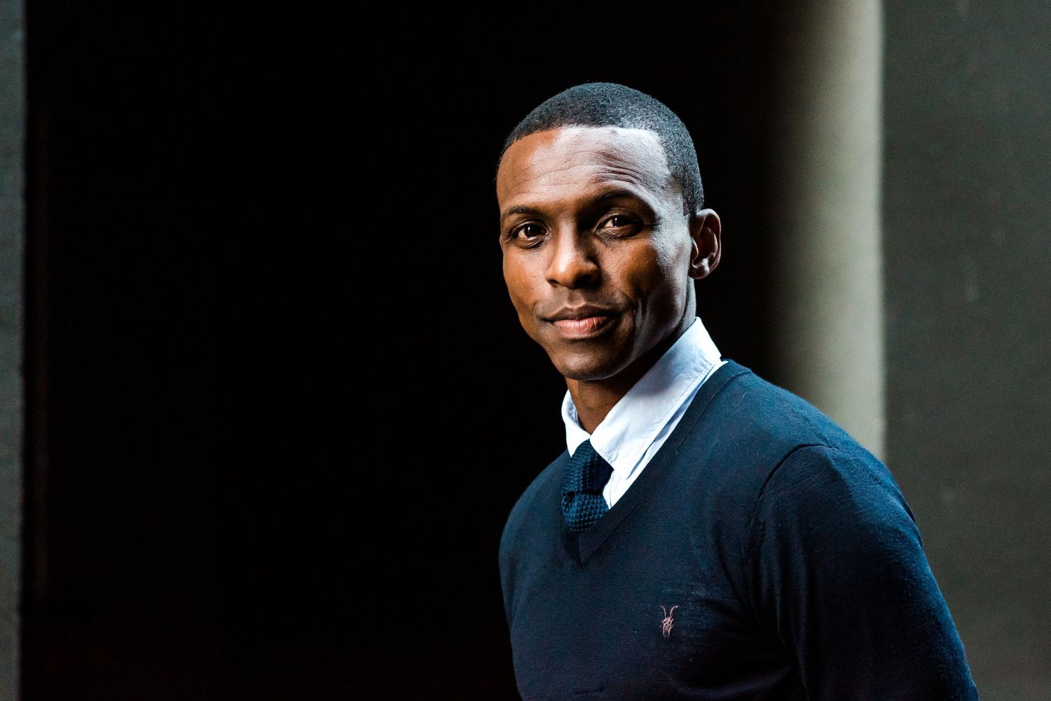 Professional portrait with dramatic side lighting against dark background.