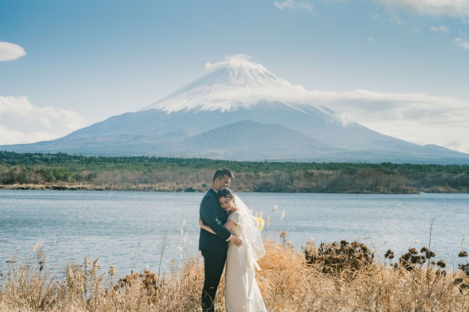 A romantic wedding photo with Mount Fuji's snow-capped peak creating a majestic backdrop over the lake.