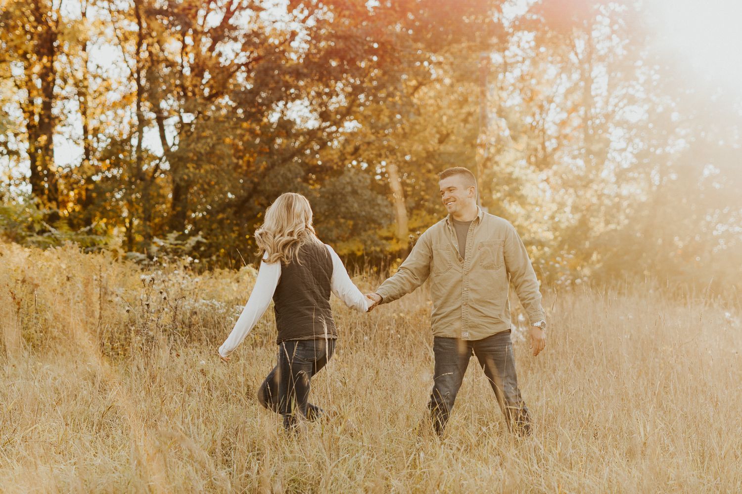 Couple walking hand in hand through golden autumn field at sunset.
