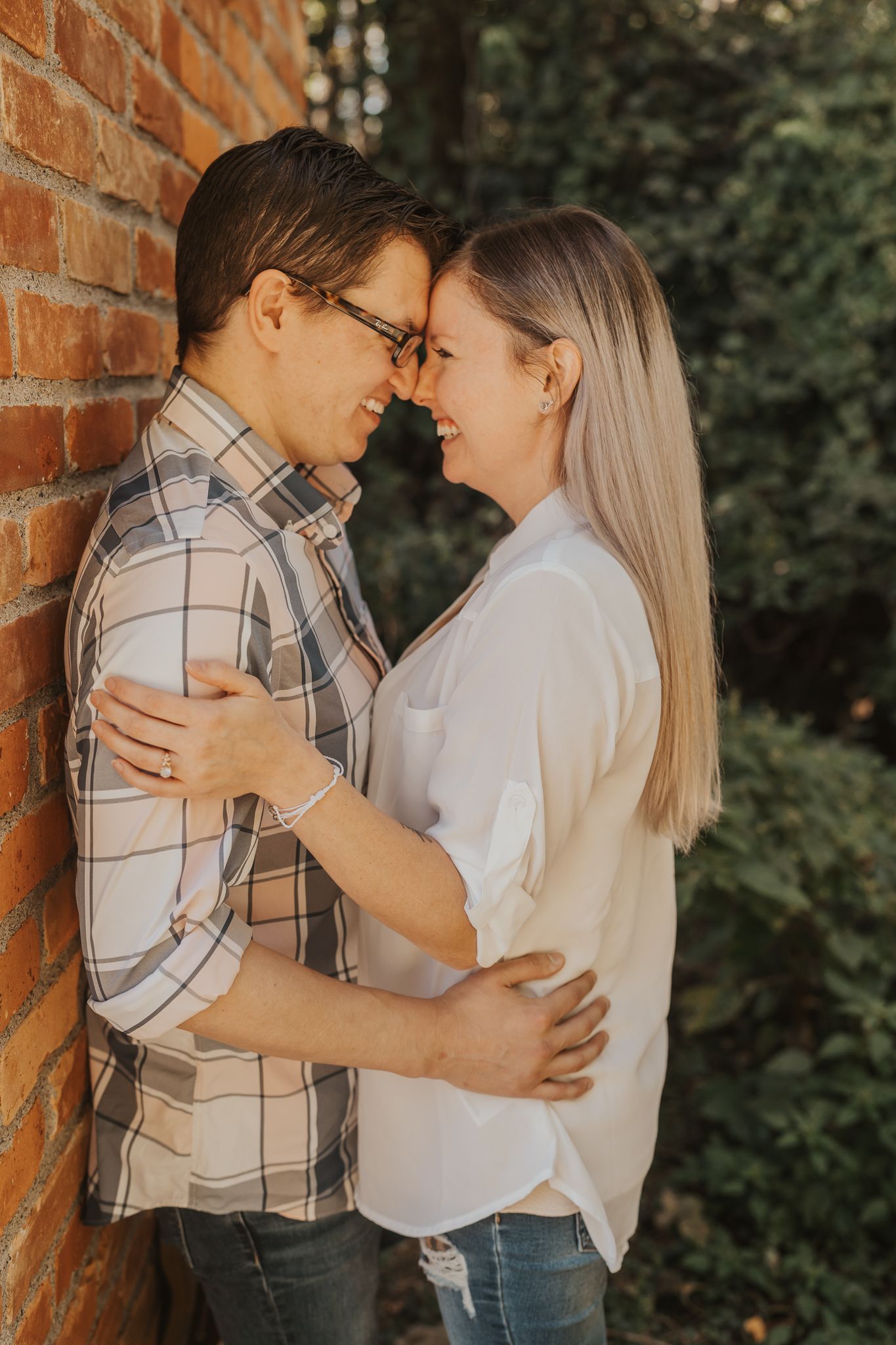 Romantic couple embracing against rustic brick wall in warm lighting.