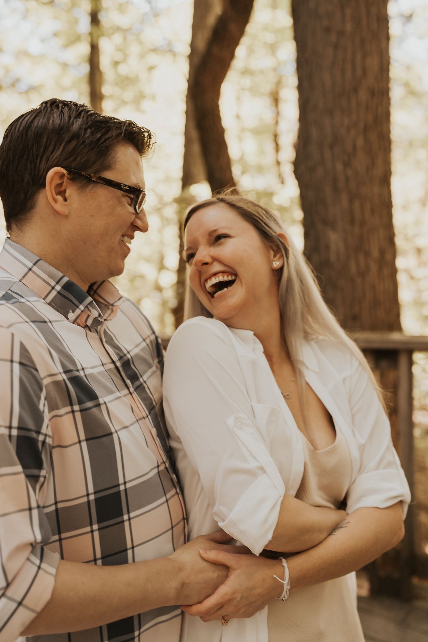 Couple sharing intimate laughing moment in sunlit wooded setting.