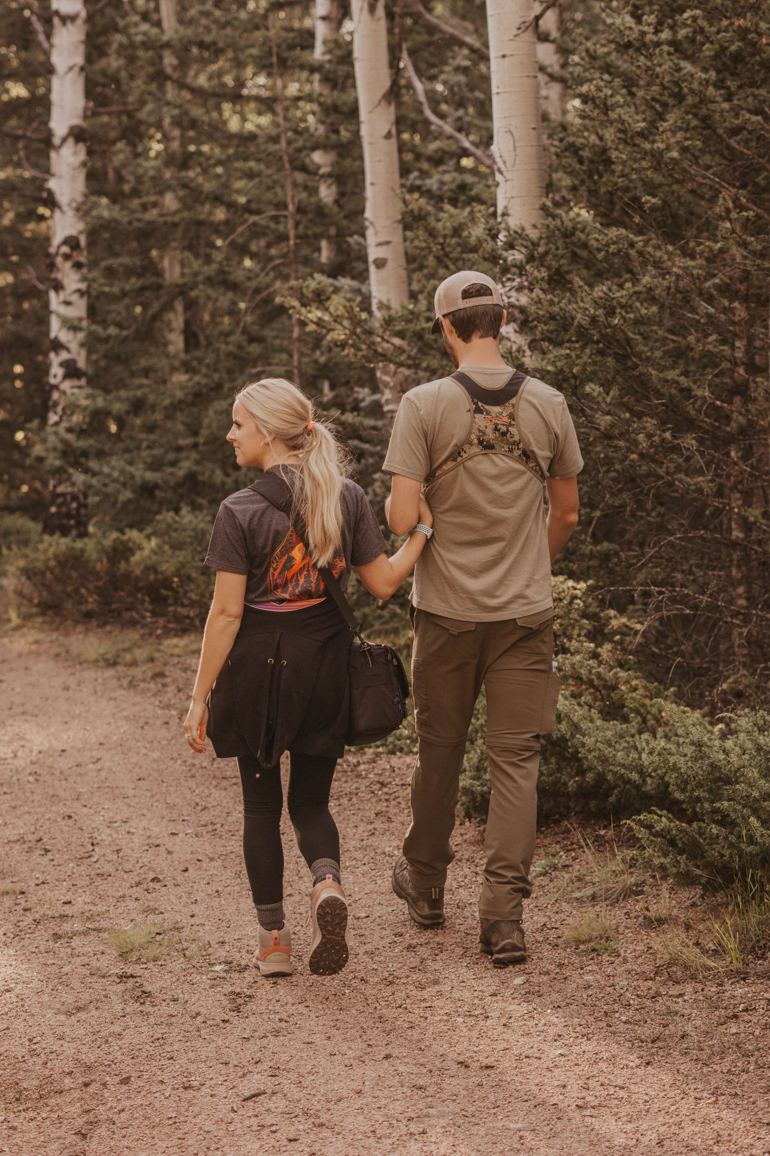 A hunting couple walks hand in hand along a forest trail during sunset taken by Michigan photographer.