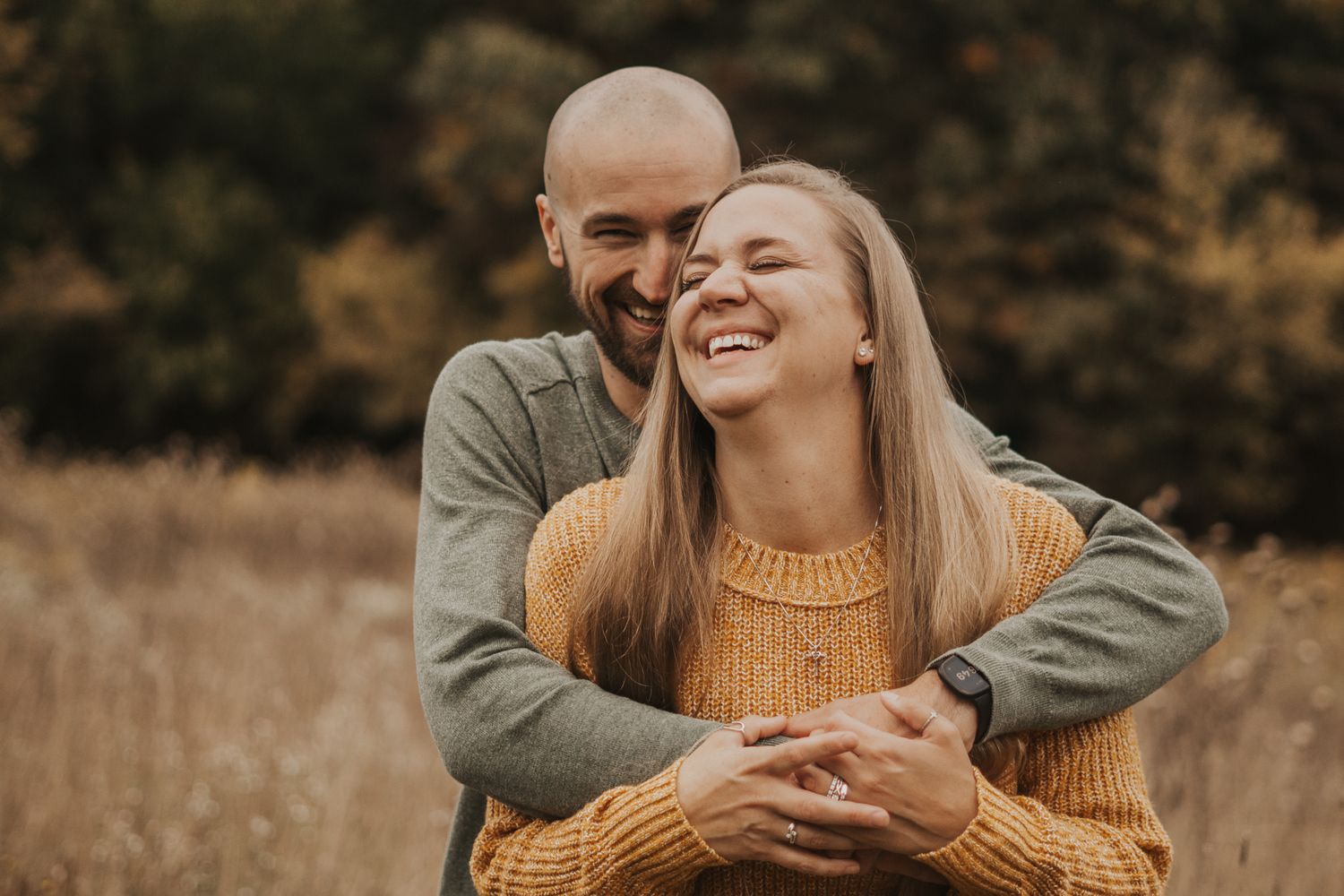 Couple sharing joyful moments in autumn field wearing cozy sweaters.