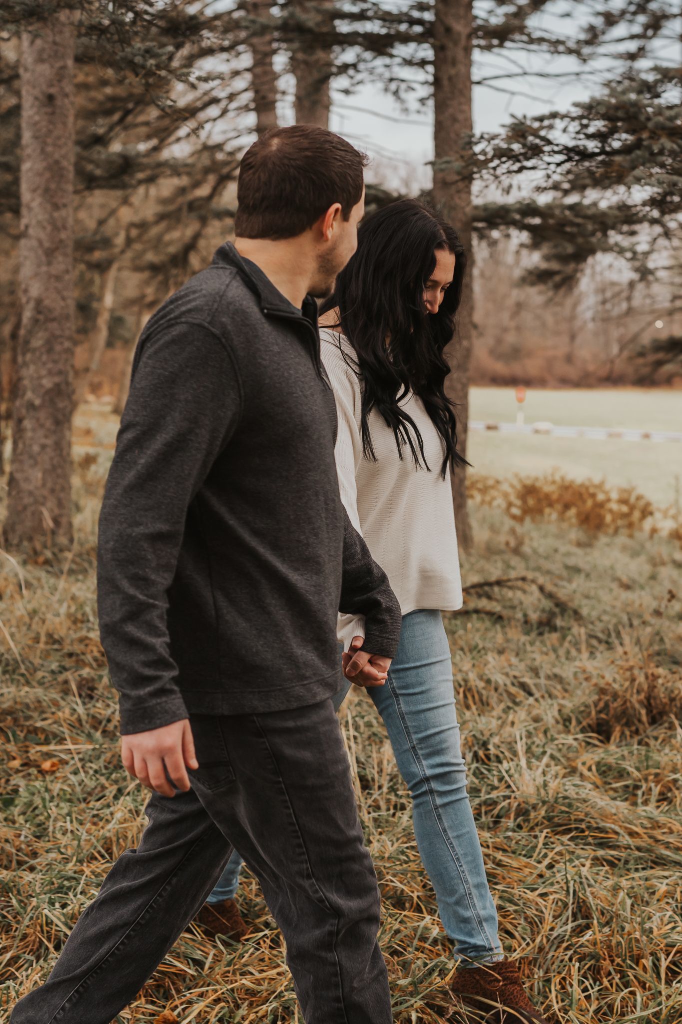 Couple playfully walking through fallen pine needles in wooded area.