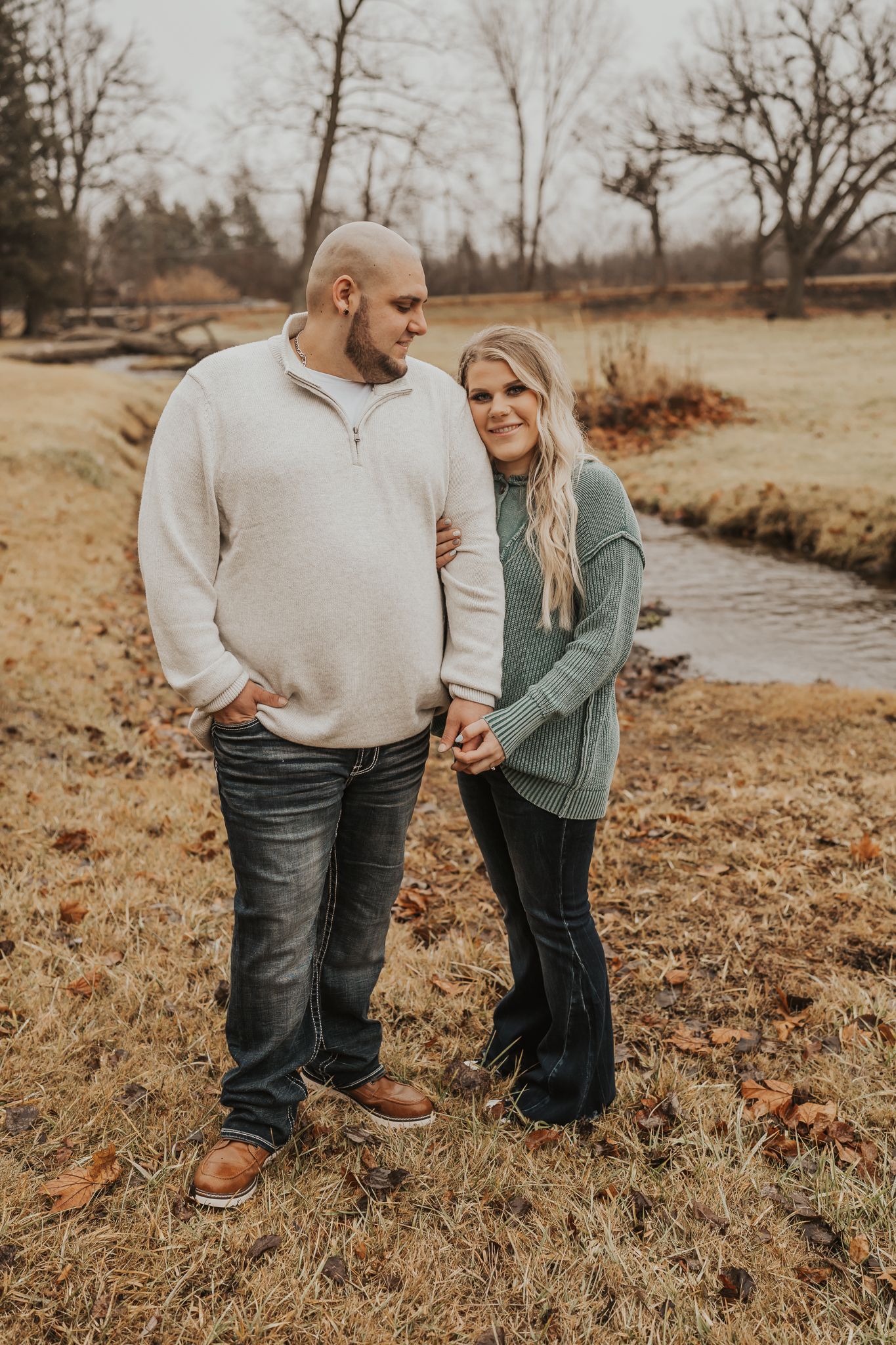 Couple standing by a stream on brown grass during autumn in Cement City Michigan.