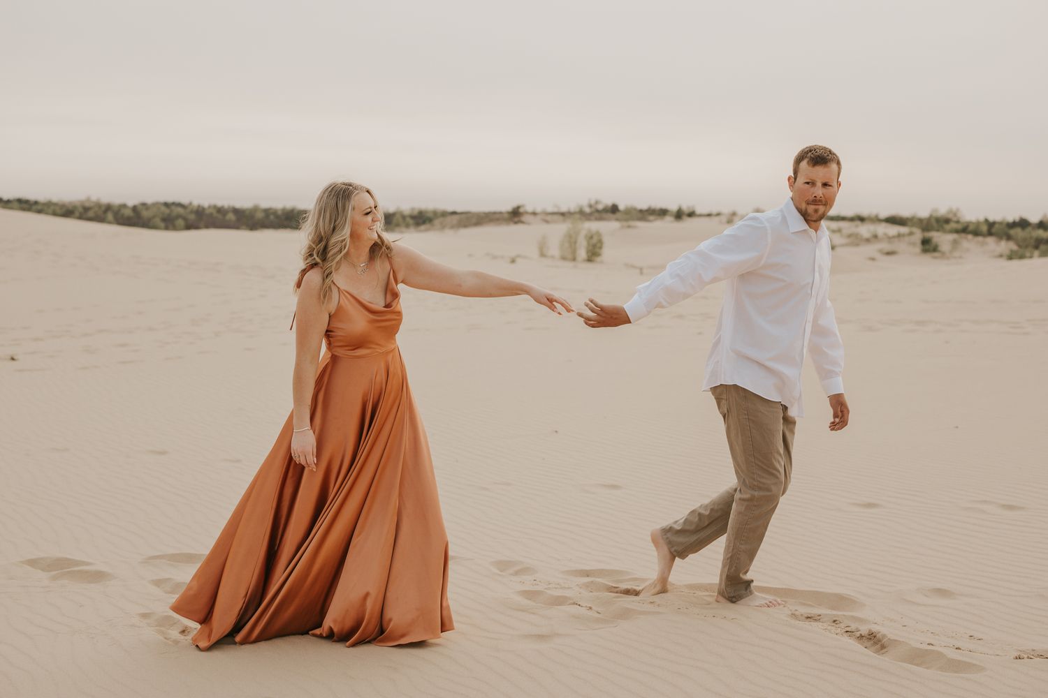 Playful couple dancing together on sandy dunes during golden hour.