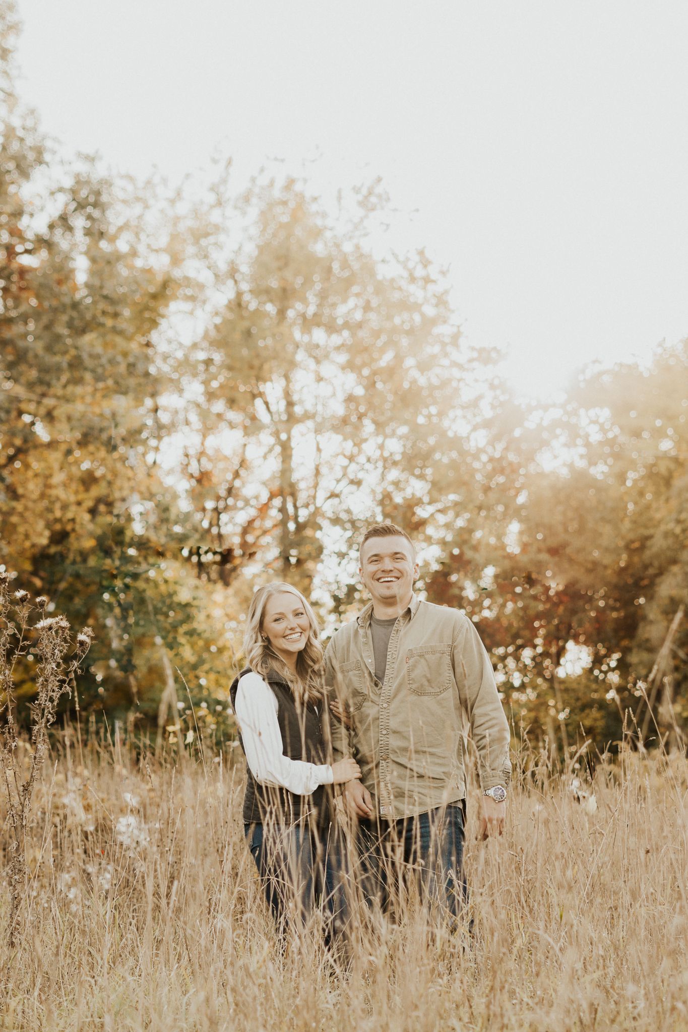 Couple walking through sunlit field during golden hour photoshoot.