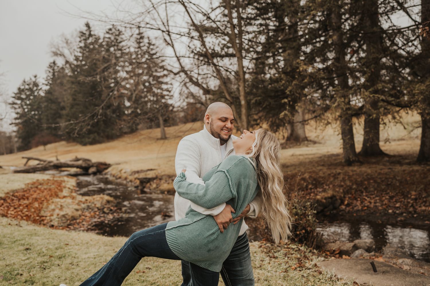 Romantic dip pose in autumn setting with stream and trees in background at Michigan's McCourtie Park.