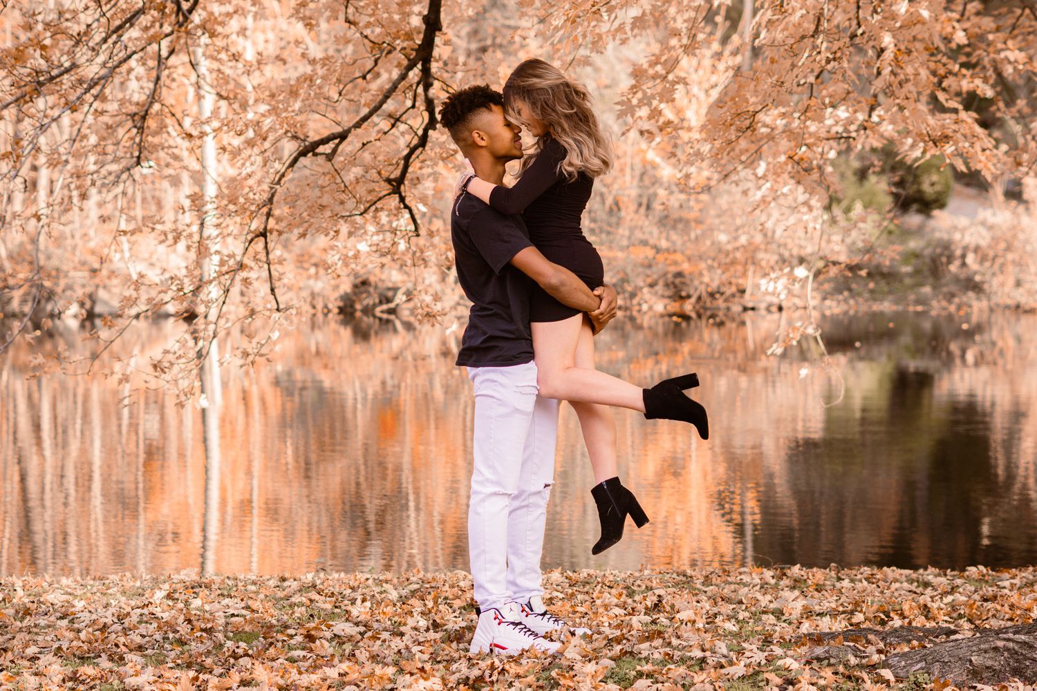Couple sharing tender moments by a lake with fall foliage in background.