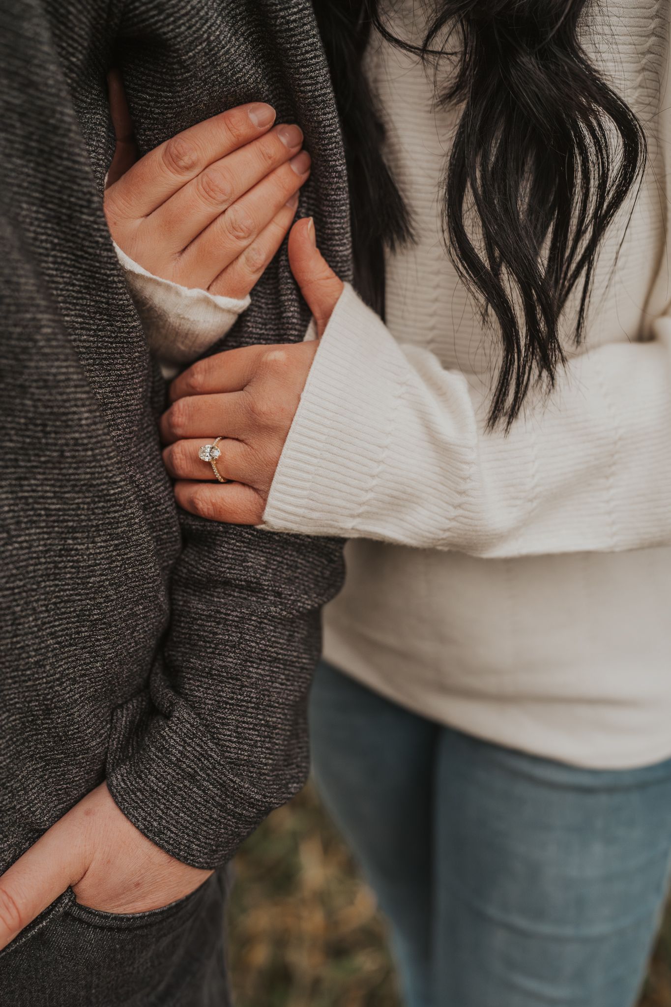 Close-up of hands clasped together wearing cozy sweaters in autumn for engagement photography.