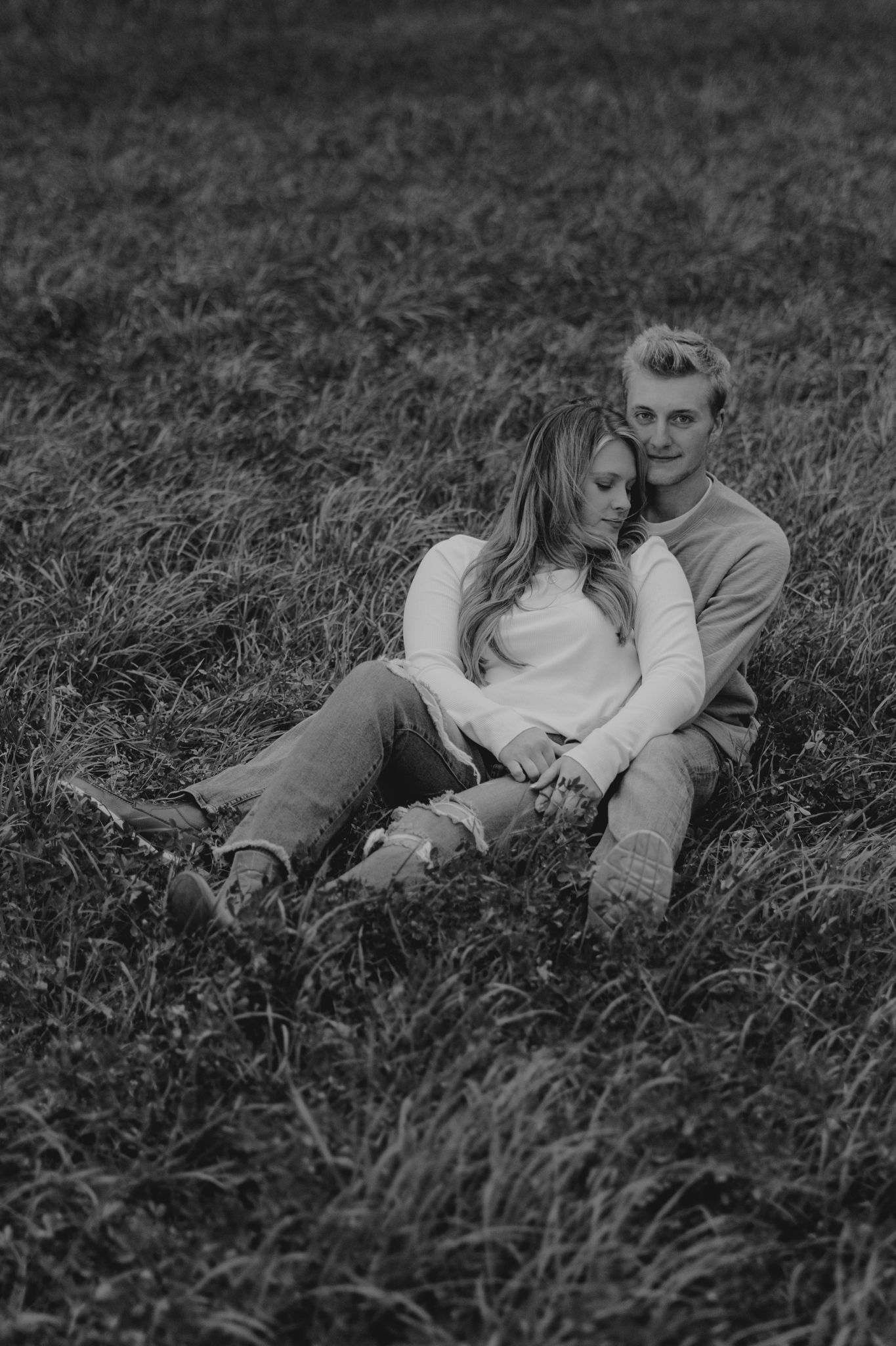 Couple lying together in tall grass during romantic black and white photoshoot.