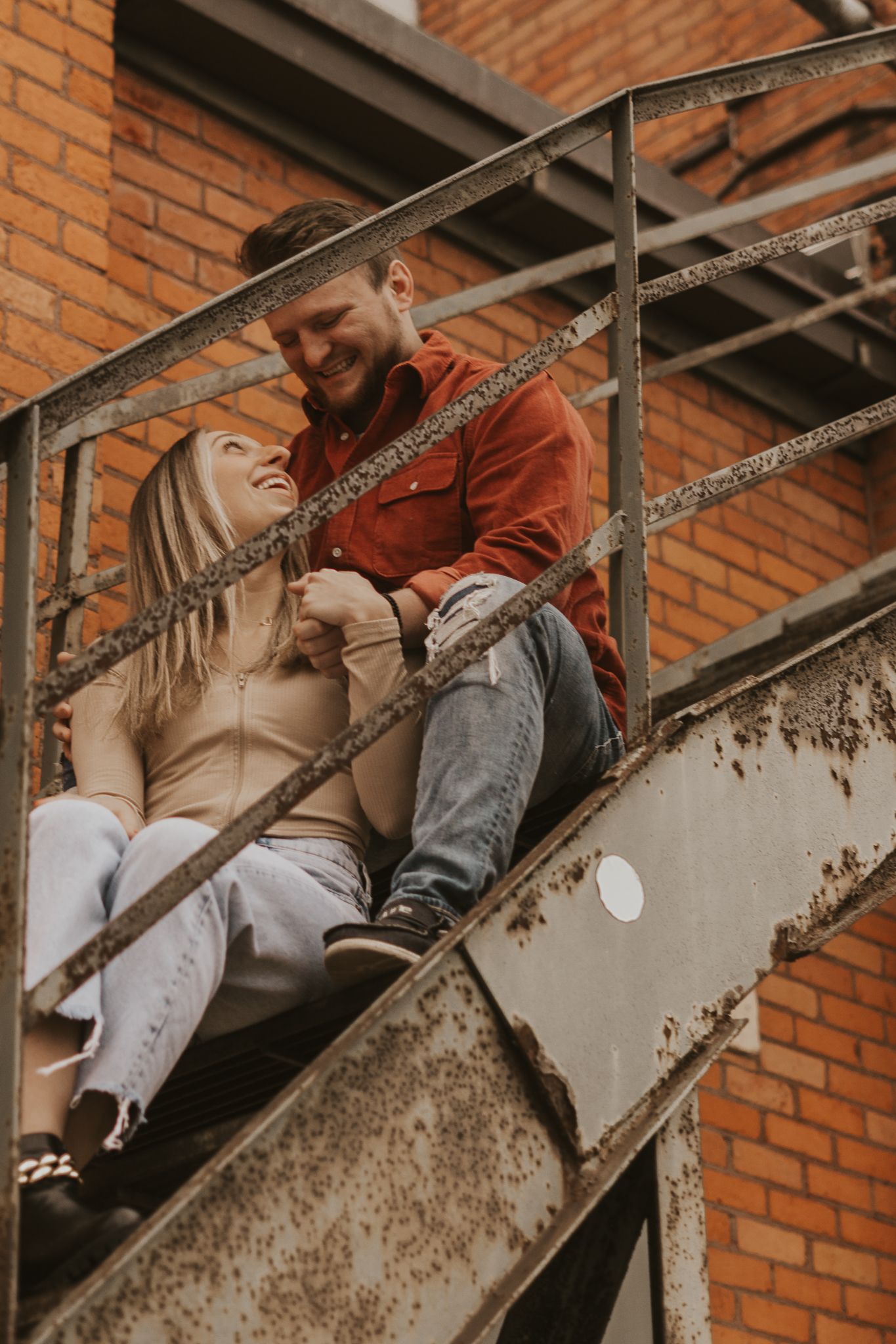 Couple sitting on industrial metal stairs against brick wall sharing romantic moments.