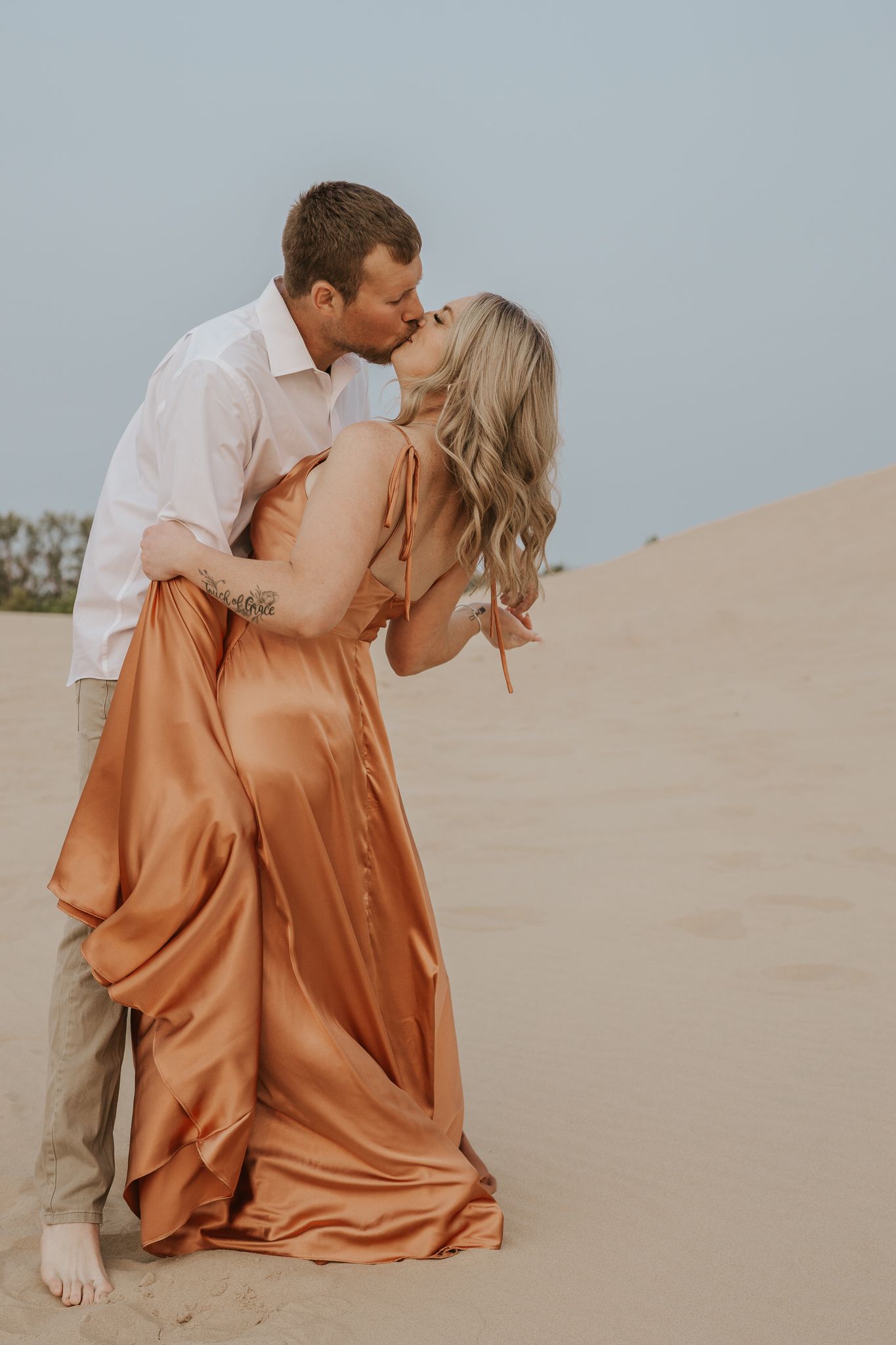 Romantic couple sharing intimate moments on sandy dunes at sunset in South Haven Michigan.