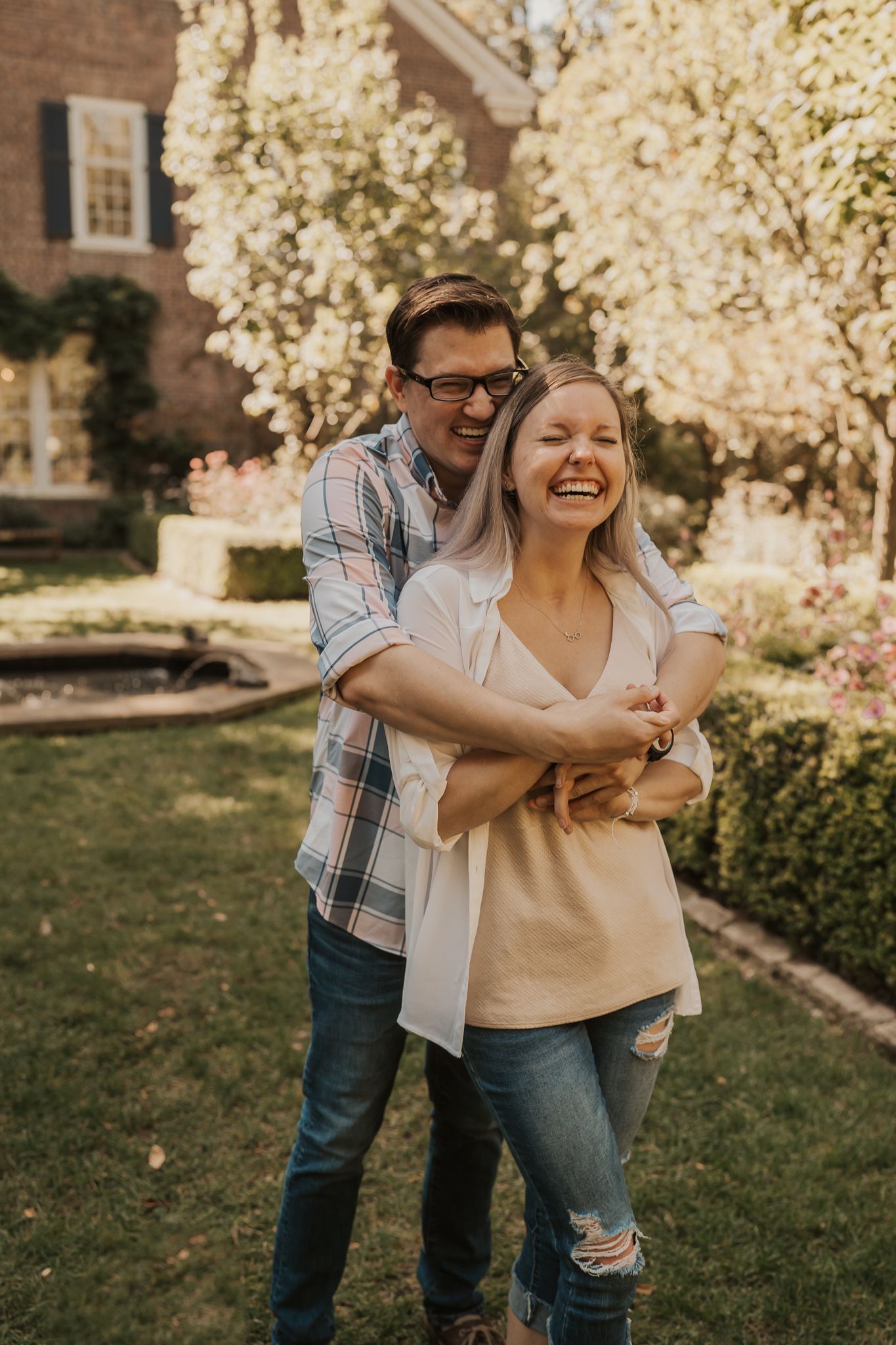 Playful couple laughing together in front of blooming spring trees.