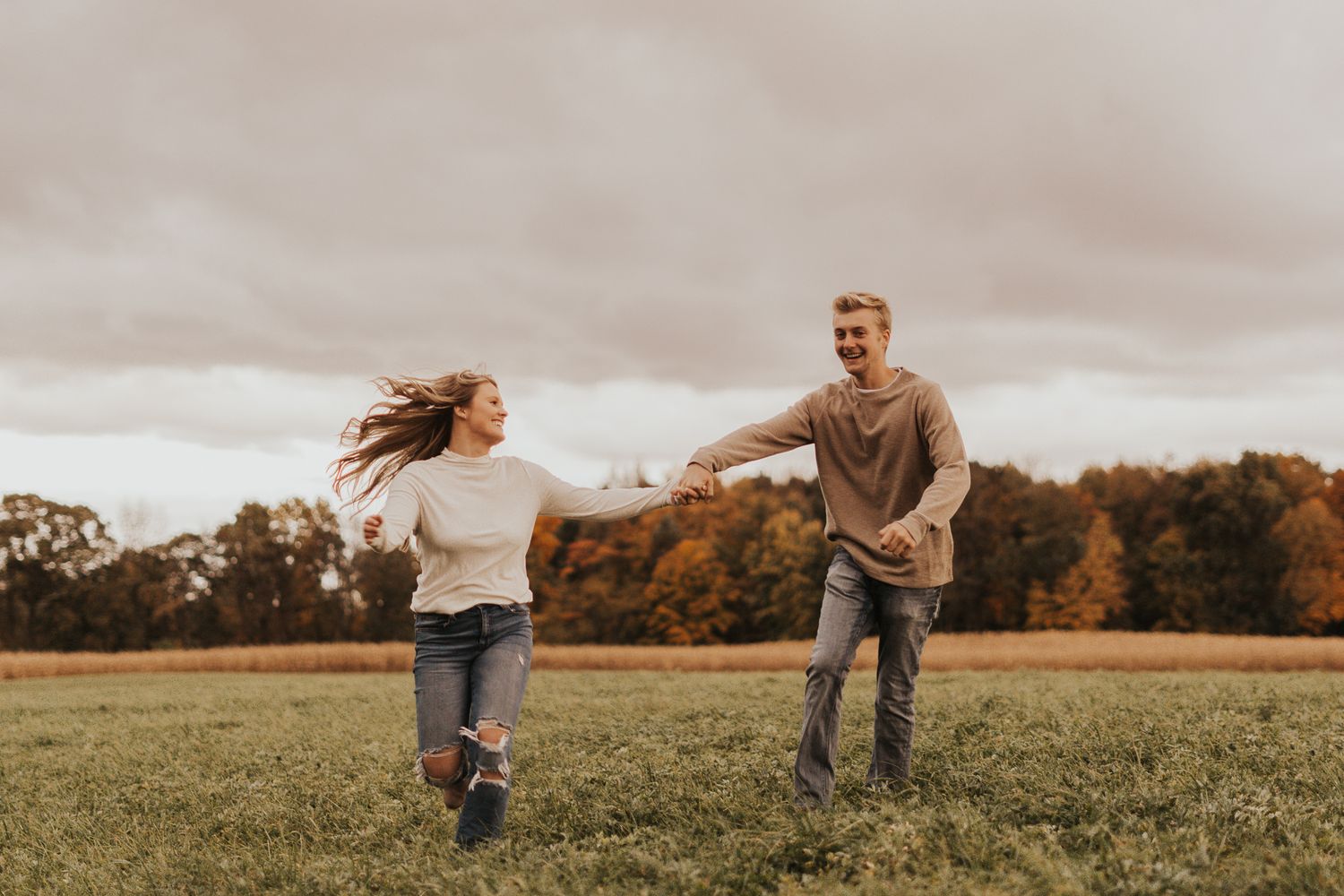 Couple running playfully through a golden field during sunset.