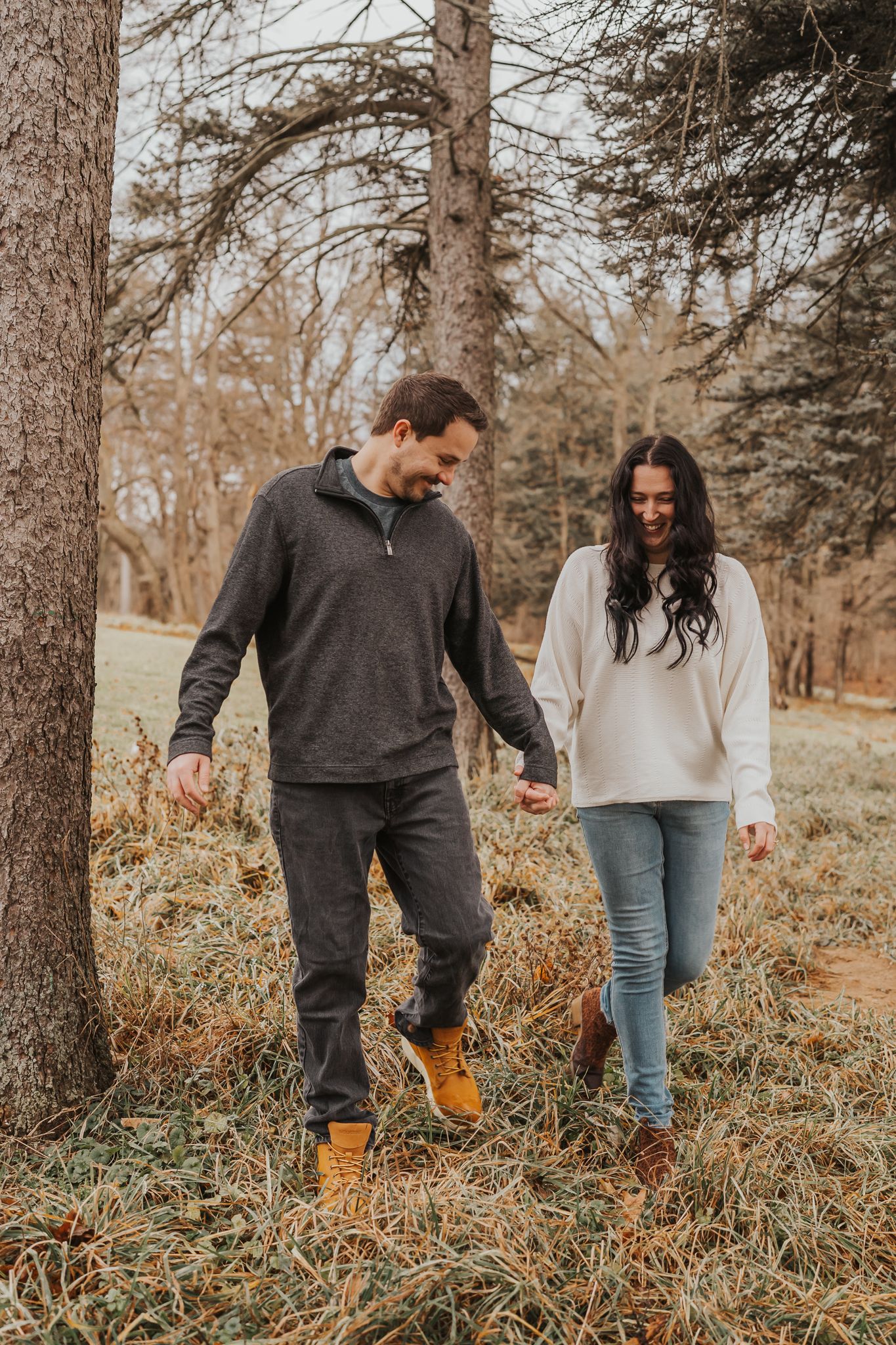 Couple walking through tall grass and pine trees in autumn setting.
