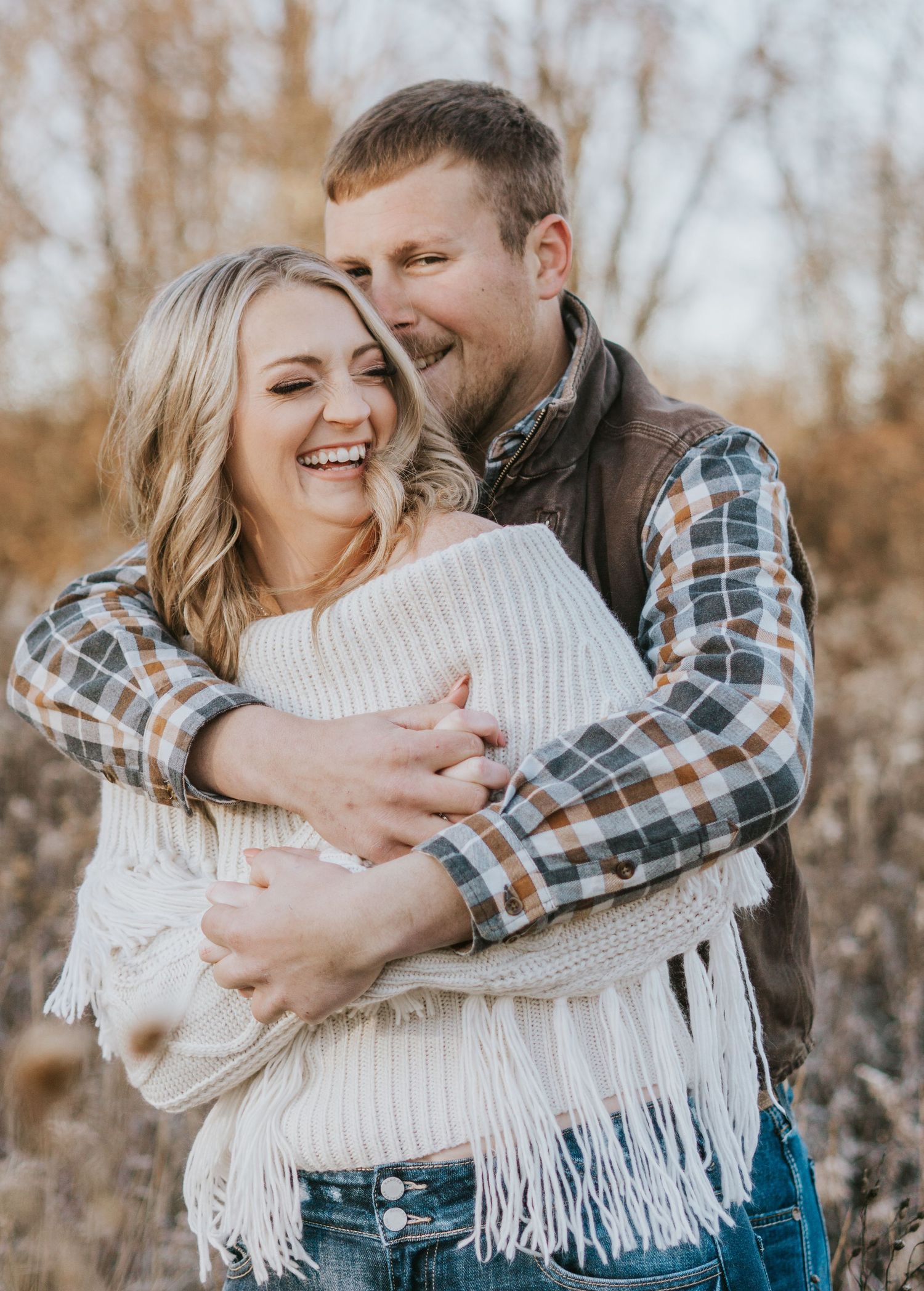 Cozy Michigan winter engagement photos showing couple embracing in cream sweater and plaid shirt.