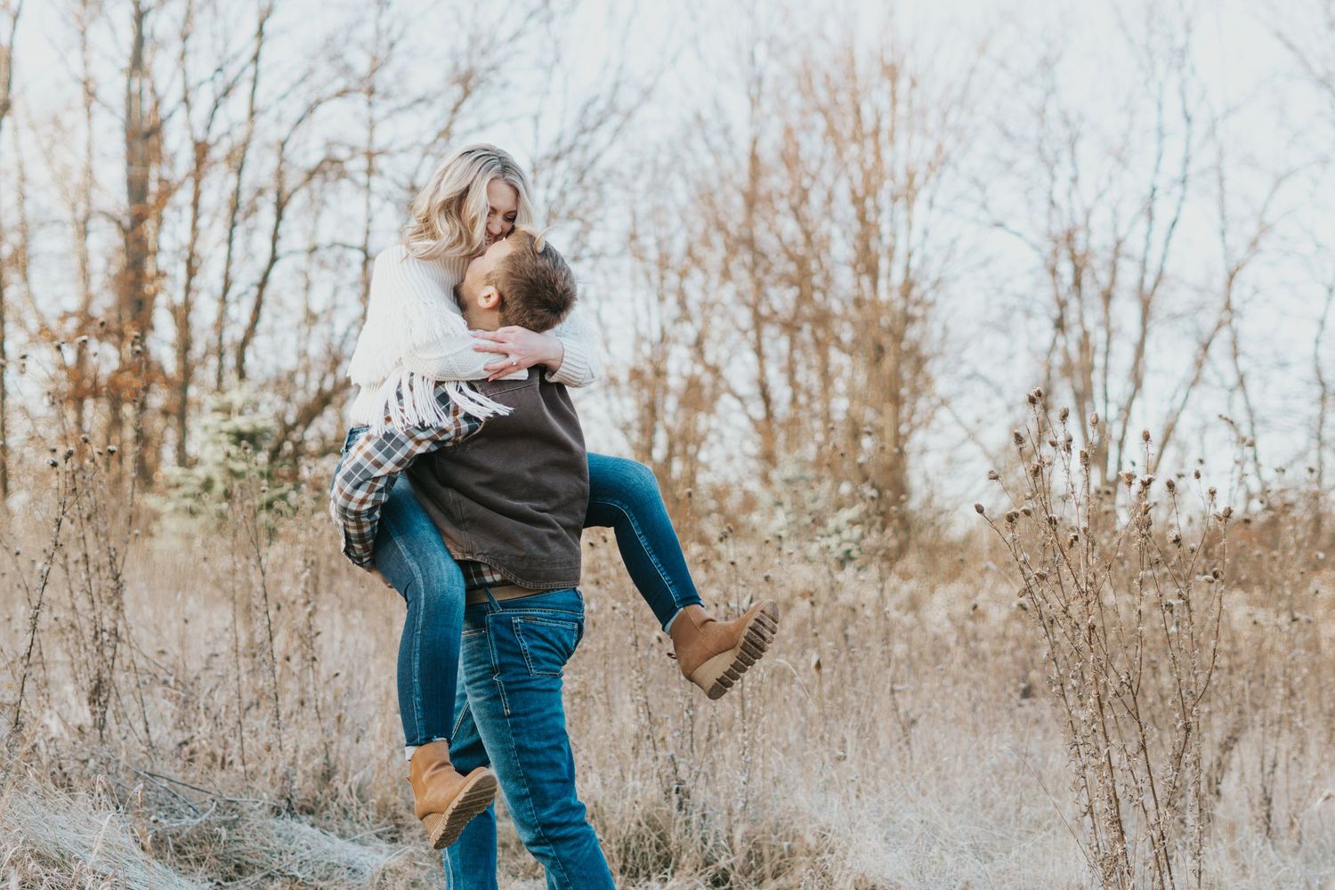 Playful couple having fun in winter setting with bare trees.