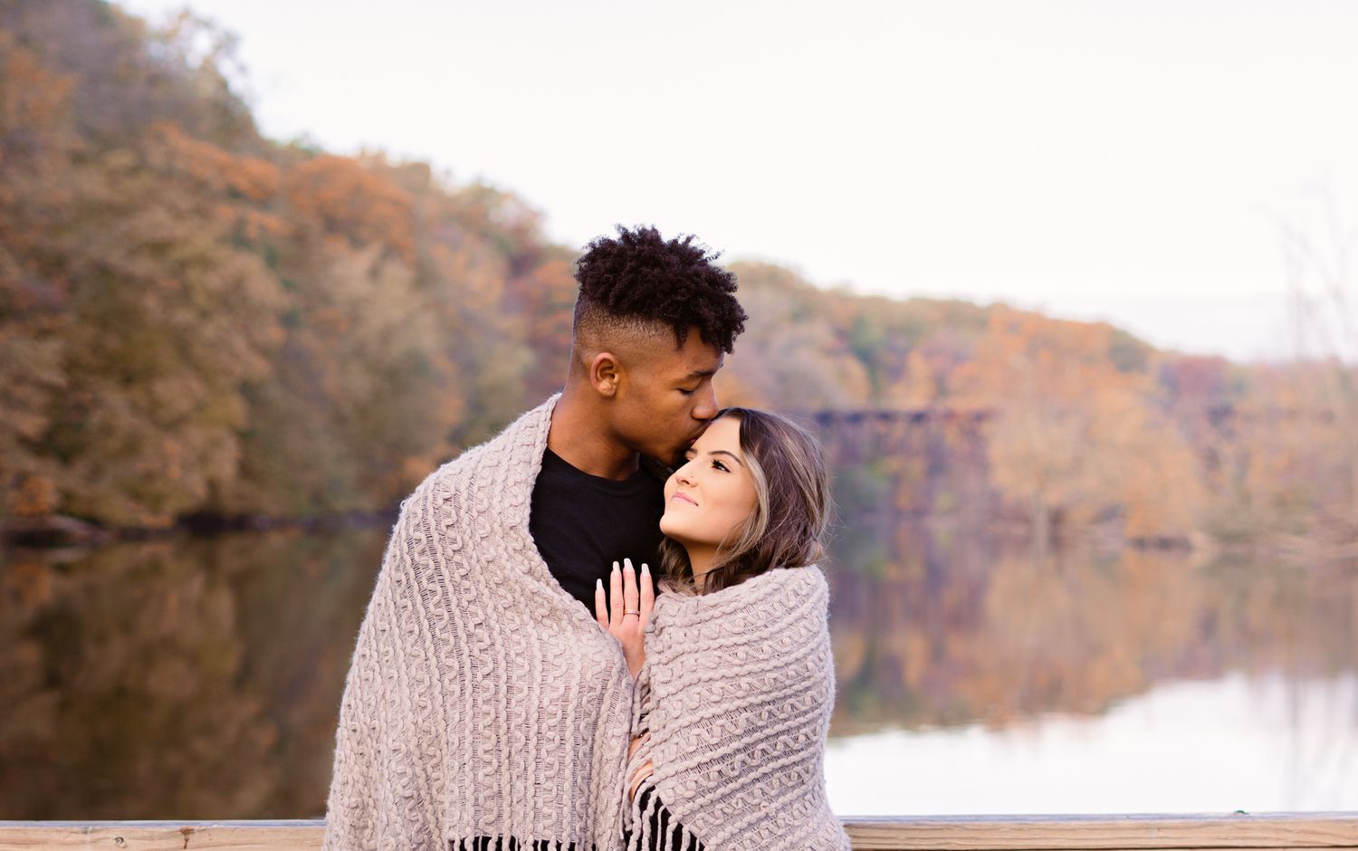 Romantic lakeside scene with couple wrapped in blanket during autumn.