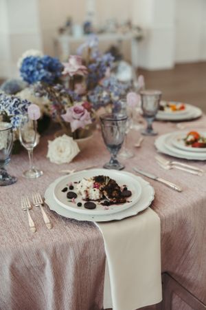 Elegant wedding table setting with blue hydrangeas and vintage glassware on dusty pink tablecloth.
