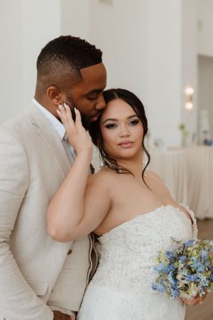 Intimate wedding portrait in bright white room with floral bouquet and elegant attire.