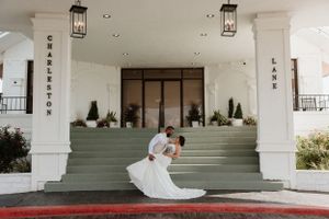 Romantic wedding dip pose on grand white entrance steps with hanging lanterns.
