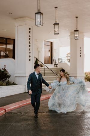 Wedding couple walks together as light blue dress flows dramatically under venue's covered entrance.