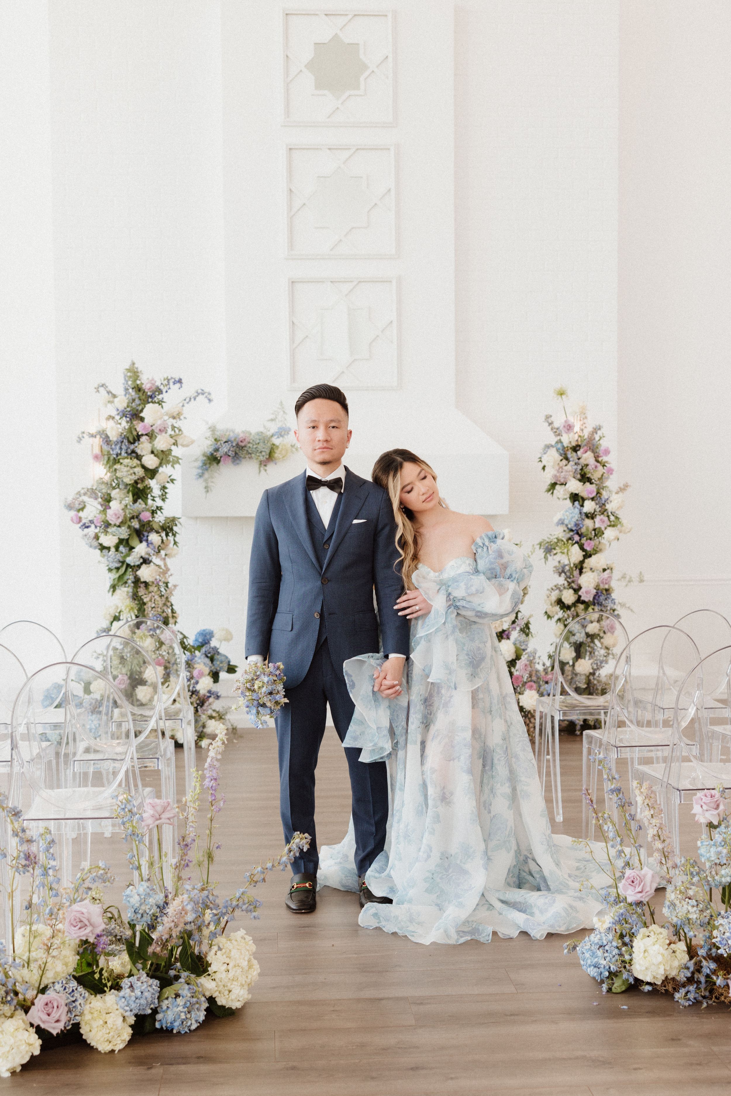 Wedding ceremony setup with floral aisle decorations and elegant couple in blue and navy attire.