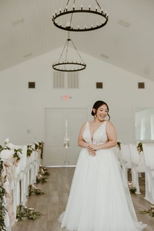 Elegant bride in flowing white gown standing in modern chapel with circular chandeliers.