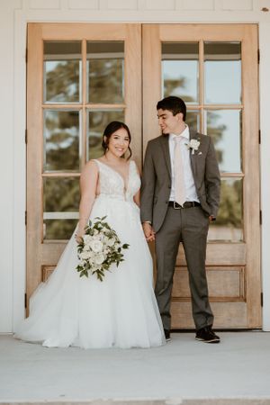 Wedding couple posing against vintage French doors with white floral bouquet.