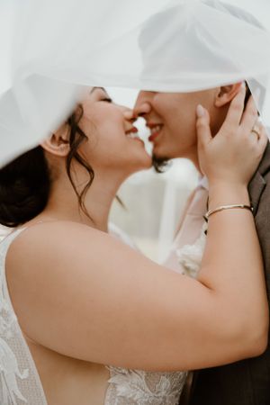Intimate wedding moment captured under flowing white veil.
