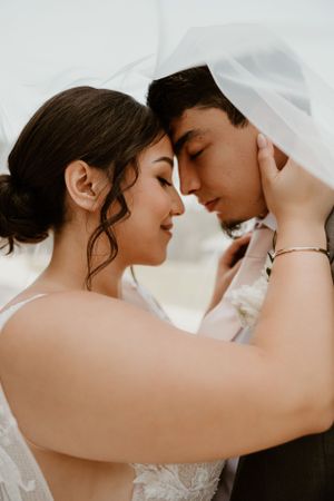 Intimate wedding portrait under a white veil showing tender romantic moment between newlyweds.