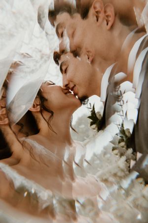 Artistic close-up wedding photo capturing romantic kiss through delicate white veil.