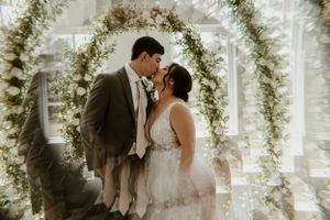 Wedding couple sharing intimate moment under floral arch with natural lighting.