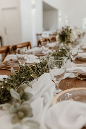 Elegant wedding reception table setting with greenery garland runner and wine glasses.