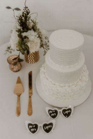 White tiered wedding cake with floral decor and heart shaped place cards on display.