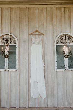 White wedding dress hanging between ornate wall sconces on a rustic wooden wall.