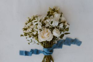 Delicate white rose bouquet tied with a blue ribbon on a light background.