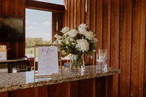 Wedding reception setup with white floral centerpiece and menu card on granite countertop.
