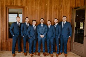 Wedding party in matching navy suits standing in front of wooden wall.