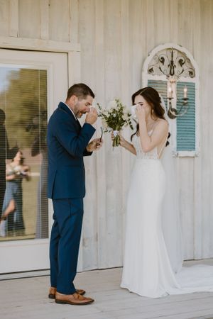 Emotional first look reaction between couple on white porch with floral details.