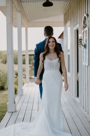 Couple walking along white porch during wedding photoshoot.
