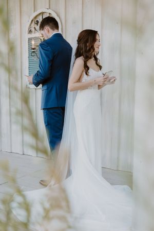 A couple stands back to back in wedding attire during a romantic first look moment.
